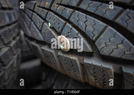 Primo piano di un usato e inutile auto pneumatico forato con un rivetto metallico Foto Stock