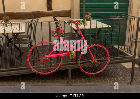 Un vecchio ciclo, dipinta in rosa e appoggiata contro la ringhiera di un ristorante e con il telaio e ruote decorato da fiori e nastri Foto Stock