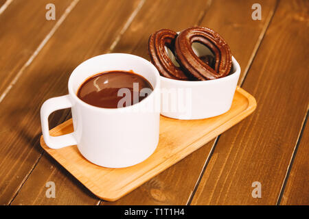 Piccolo spagnolo frittelle di cioccolato servita su un tavolo di legno con una tazza di cioccolato caldo Foto Stock