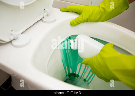 Uomo in gomma guanti protettivi pulizia, lavaggio wc con spazzola e bottiglia di agente di pulizia in mani. Verde detergente liquido di gocciolamento in wc Foto Stock