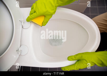 Uomo in gomma guanti protettivi pulizia, lavaggio wc con spazzola e bottiglia di agente di pulizia in mani. Verde detergente liquido di gocciolamento in wc Foto Stock