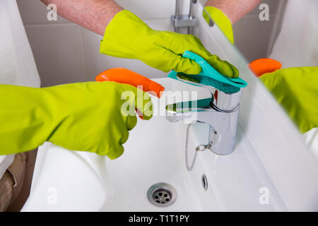 Uomo in gomma guanti protettivi per la pulizia e la lucidatura lavello e rubinetto. Superficie lucida del rubinetto di acqua, mani con spugna e bottiglia di agente di pulizia. Foto Stock