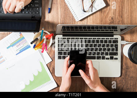 Due persone che lavorano in ufficio, la digitazione e utilizzando laptop, vista dall'alto, piatto laici. Smart guarda sulla mano e smart phone sul tavolo. Tazza da caffè Foto Stock