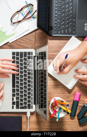 Due persone che lavorano in ufficio, la digitazione e utilizzando laptop, vista dall'alto, piatto laici. Smart guarda sulla mano e smart phone sul tavolo. Tazza da caffè Foto Stock