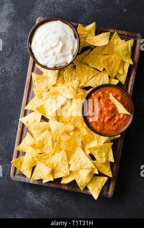 Nachos corn chips con pomodoro piccante e formaggio salse. Cibo messicano concetto. Mais giallo totopos chips con salsa di salsa. Vista dall'alto. Foto Stock