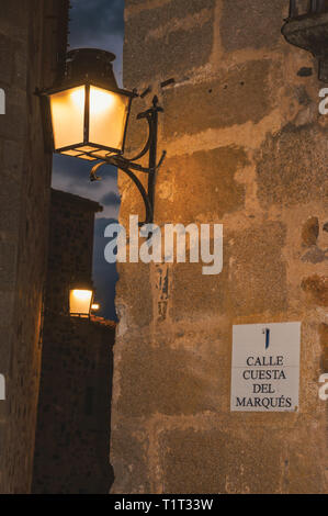 Vecchio stile applique in metallo attaccato al muro di pietra e di luce morbida in un vicolo al crepuscolo in Caceres. Un villaggio pieno di vecchi edifici in Spagna. Foto Stock