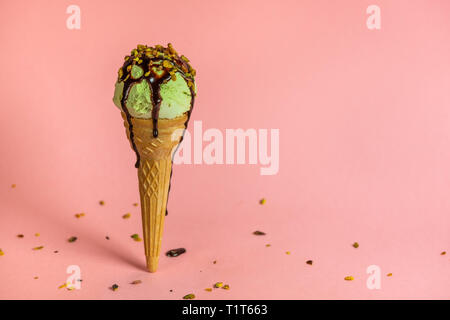 Strano concetto creativo instabile con pistacchio cono gelato con salsa di cioccolato e noci era cosparsa su sfondo rosa Foto Stock