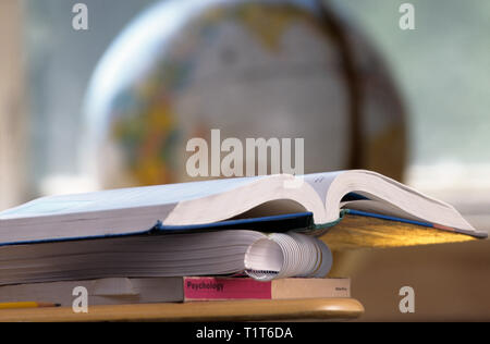 Una scuola aperta di un libro di testo è visto seduto su altri libri. In fondo è un globo. Inquadratura orizzontale. Foto Stock