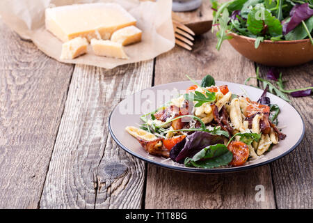 Fatti a mano fusilli con pancetta arrosto pomodori ciliegia e fresche verdure verdi e rabboccato parmigiano grattugiato su tavola in legno rustico, chiudi Foto Stock