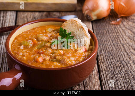 Una sana vegetariana zuppa di orzo con verdure di stagione in vaso in ceramica su tavola in legno rustico, a base di vegetali alimentari, vicino il fuoco selettivo Foto Stock