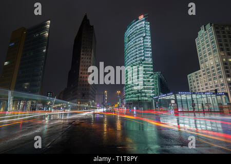 Accesa alti edifici moderni, cars' luce sentieri, strade bagnate e ingresso alla stazione ferroviaria a Potsdamer Platz nel centro di Berlino, Germania, al tramonto. Foto Stock