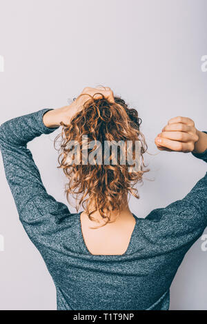 Vista posteriore della giovane donna con capelli ricci facendo la sua coda di cavallo acconciatura. Foto Stock