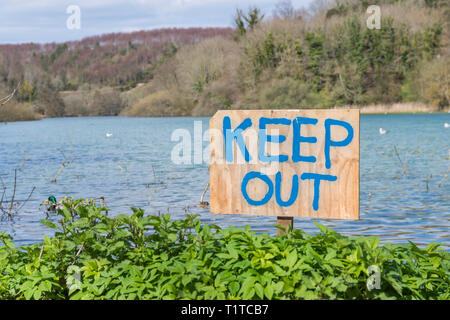Tenere fuori firma scritta a mano su un cartello in legno infissa a terra da un lago. Foto Stock