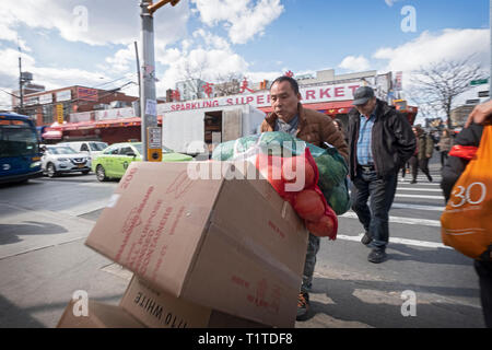 Un americano asiatico uomo muove il cibo e i pacchetti da un luogo ad un altro su Main Street a Chinatown, il centro cittadino di lavaggio, Queens, a New York City Foto Stock