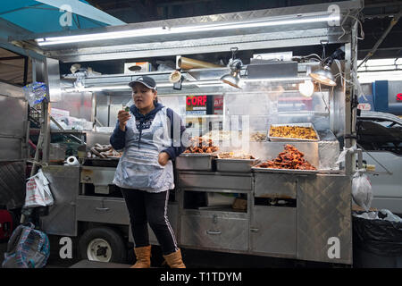 Un Sud Americana donna vendita di carni alla griglia e altri alimenti da un carrello sotto la sopraelevata treni della metropolitana . In corona, Queens, NYC Foto Stock