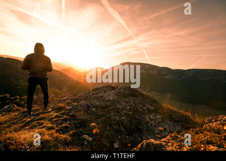 L uomo sta sul picco di una montagna e guardando a Sun. bel momento il miracolo della natura durante il tramonto in Austria Foto Stock