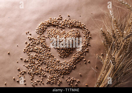 Erba di frumento semi in forma di cuore e di spezie di grano su sfondo rustico. Amore di fibra sana nozione di cibo. Foto Stock