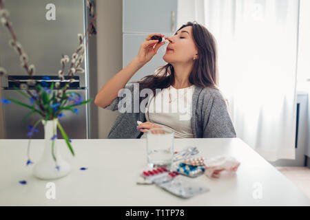 Allergia a molla. Stanco della donna utilizzando gocce nasali contro allergie stagionali e assunzione di pillole su cucina a casa. Sanità e medicina Foto Stock