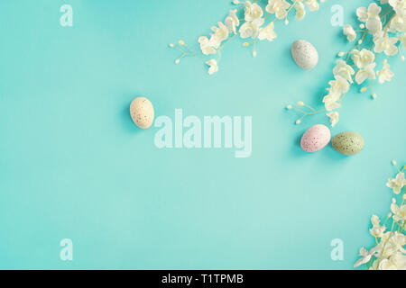 Pastello uova di Pasqua e fiore bianco blossoms oltre un teal sfondo blu con camera per copiare lo spazio. Immagine ripresa dalla vista dall'alto. Foto Stock