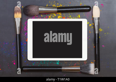 Piatto di laici touchpad con pennelli per il trucco su sfondo nero Foto Stock