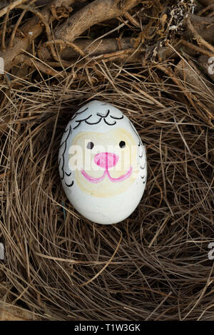 Detail of painted Easter egg with face of sheep in a birds nest. Foto Stock