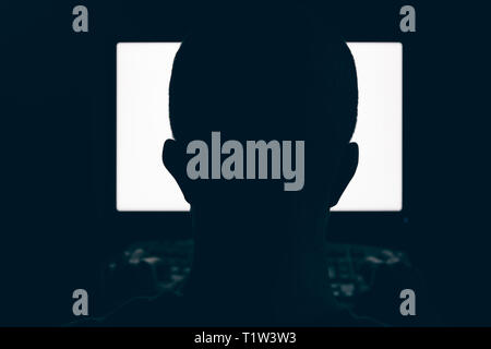 Silhouette di uomo testa nella parte anteriore del monitor per computer la luce nella stanza buia Foto Stock