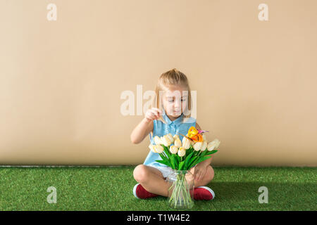 Bambino seduto con le gambe incrociate, guardando i fiori e la cattura di butterfly Foto Stock