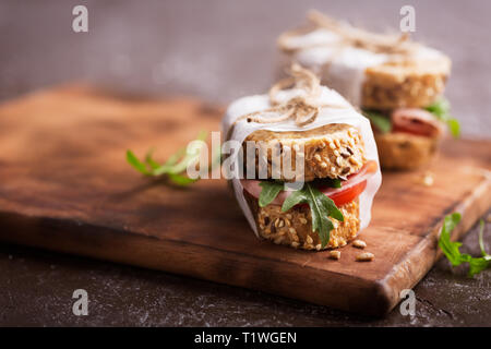 Panini fatti in casa con prosciutto, pomodori e verdura fresca insalata spruzzata con olio di oliva. Il cibo sulla lavagna scuro Foto Stock