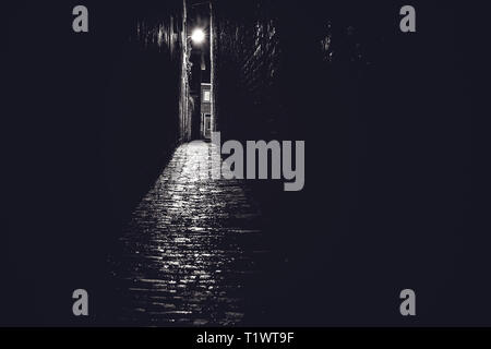 Illuminato atmosferica vecchia strada durante la pioggia con acqua riflettente scende sulla strada Foto Stock