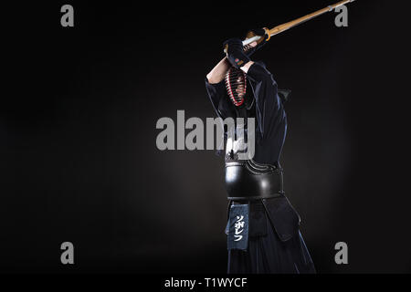 Combattente di Kendo nel casco tradizionale pratica con la spada di bambù su nero Foto Stock