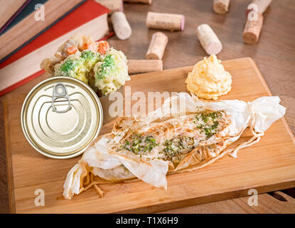 Piccante di spigola con verdure cotte e purè di patate servita in un cuoco carta su una tavola di legno. Foto Stock