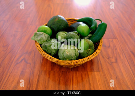 Ingredienti per la salsa di avocado in un cesto tessuto su una superficie in legno: avocado, tomatillos, jalapeños. Foto Stock