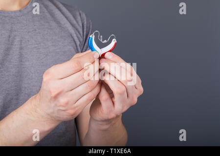 Primo piano delle mani che tengono poco appariscente piccoli apparecchi acustici in forma di cuore, come persone non udenti ne ha bisogno. Uomo con apparecchi acustici, closeup. Apparecchi acustici Foto Stock