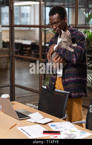 Uomo con un gatto nelle sue mani sul suo luogo di lavoro Foto Stock