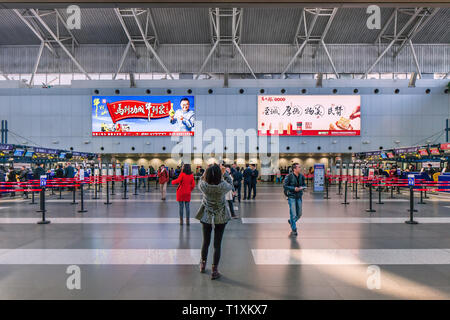 Aeroporto di Pechino T2 interno con cartelloni, contatori e viaggiatori. La donna è fotografare con smart phone. Foto Stock