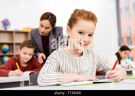 Carino lo zenzero schoolgirl iscritto in notebook durante la lezione in aula Foto Stock