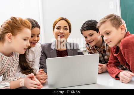 Maestro sorridente e gli studenti usando computer portatile durante la lezione in aula Foto Stock