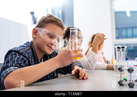 Gli alunni di occhiali di protezione bicchieri di contenimento durante la lezione di Chimica Foto Stock