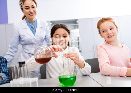 La scolaretta sorridente con bicchieri facendo esperimento chimico durante la lezione di Chimica Foto Stock