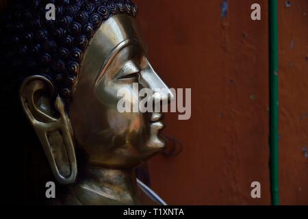 Close up di ottone statua di Buddha che mostra la faccia nel profilo con espressione calma e ricco di sfumature metalliche e le texture Foto Stock