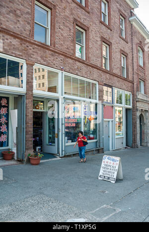 Una donna asiatica passeggiate su un marciapiede lungo vetrine del negozio in Seattle International District, a Washington. Foto Stock