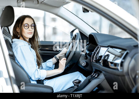 Ritratto di un giovane fiducioso donna seduta sul sedile di guida di una macchina moderna Foto Stock