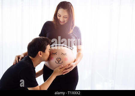 Giovane marito baciare sulla moglie incinta il disegno della pancia con cura. Foto Stock