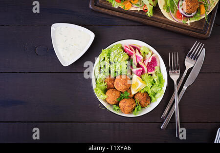 Falafel e verdure fresche. Ciotola di Buddha. Medio orientale o piatti arabi su uno sfondo scuro. Cibo Halal. Vista dall'alto. Spazio di copia Foto Stock