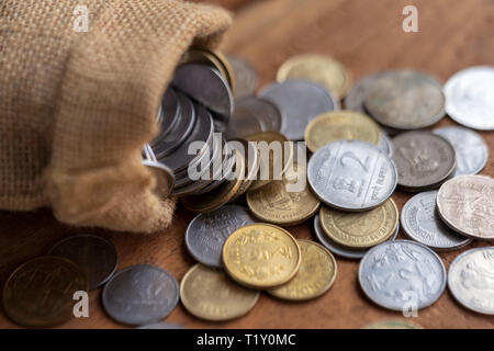 Monete indiano la fuoriuscita da un sacco di tela su una superficie di legno. La valuta indiana il concetto di sfondo. Foto Stock