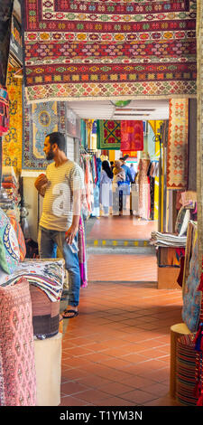 Uomo in piedi nel portico rivestita con i tradizionali tappeti e tessuti su display in Arab Street Kampong Glam Singapore Foto Stock