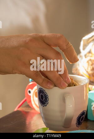 Caucasica dunking mano a Rusk in un inizio di tazza di caffè al mattino immagine con spazio copia in formato verticale Foto Stock