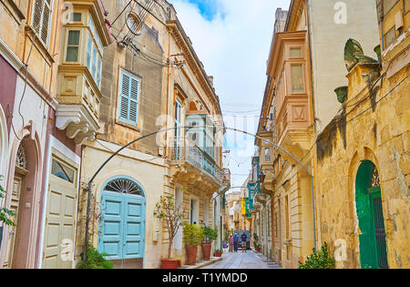 RABAT, Malta - 16 giugno 2018: la strada panoramica della città vecchia con numerose piante verdi in vaso, legno luminoso balconi Maltese, porte e scolpito ston Foto Stock