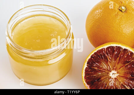 Miele all'arancio in vaso con arance tagliate da sopra. primo piano Foto Stock