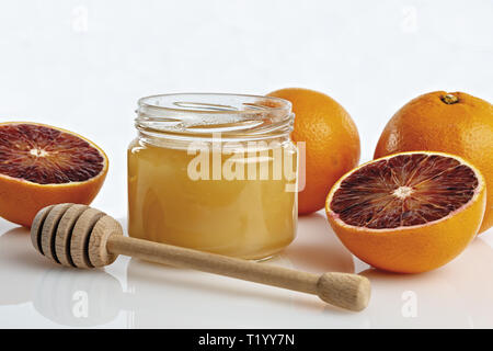 Miele all'arancio in vaso con arance tagliate. primo piano con cucchiaio Foto Stock